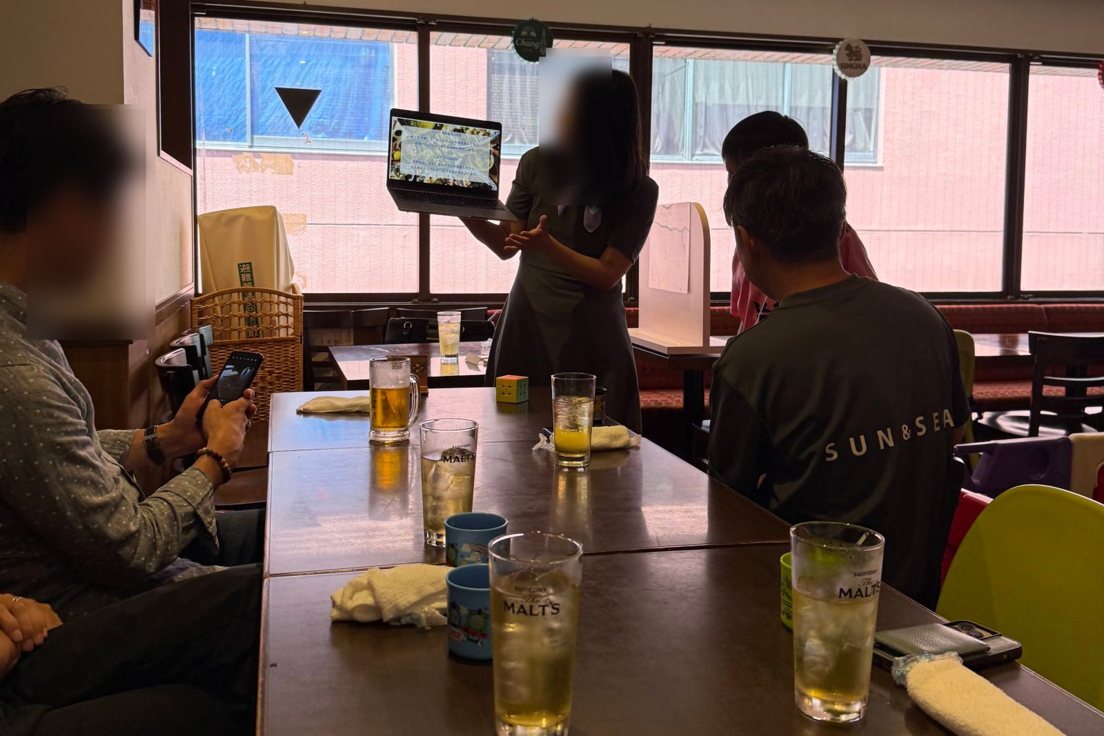 A guide shows photos on a laptop to passengers around a table, Shinjuku 2025